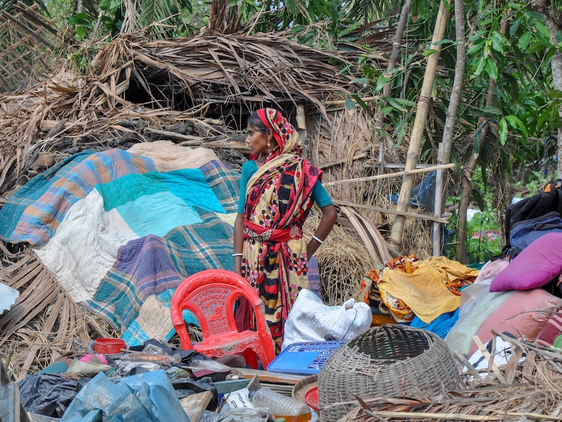 Une femme se tient au milieu des débris d’une maison.