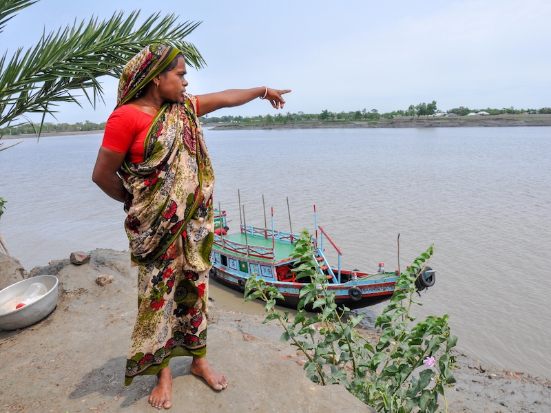 Une femme portant un sari pointe en direction de la rivière.