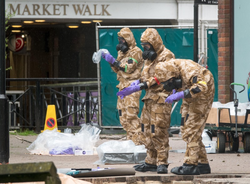 Trois militaires revêtus de tenues de décontamination s'affairent sur un site dans le quartier commerçant de Maltings, à Salisbury, en Angleterre, le 25 avril 2018, près du banc où Sergueï Skripal et sa fille ont été retrouvés.