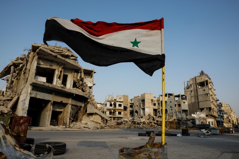 Un drapeau syrien flotte devant des bâtisses en ruine à un point de contrôle militaire dans le secteur d'al-Khalidiya, dans la partie de Homs contrôlée par le gouvernement syrien, le 18 septembre 2018.