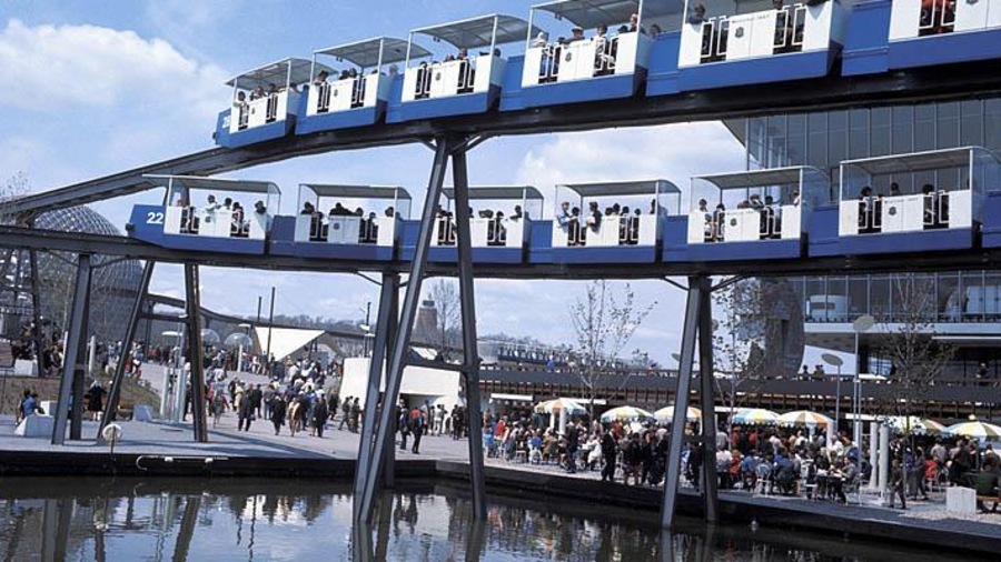 Une photo montrant deux monorails sur des rails superposés, devant le pavillon de l'URSS, avec le pavillon des États-Unis en arrière-plan. Une photo montrant deux monorails sur des rails superposés, devant le pavillon de l'URSS, avec le pavillon des États-Unis en arrière-plan.