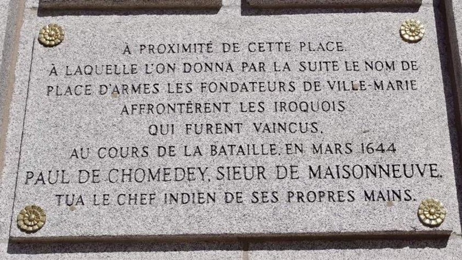 On peut lire : « À proximité de cette place à laquelle l’on donna par la suite le nom de place d’Armes, les fondateurs de Ville-Marie affrontèrent les Iroquois qui furent vaincus. Au cours de la bataille en 1644, Paul de Chomedey, sieur de Maisonneuve tua le chef indien de ses propres mains. » On peut lire : « À proximité de cette place à laquelle l’on donna par la suite le nom de place d’Armes, les fondateurs de Ville-Marie affrontèrent les Iroquois qui furent vaincus. Au cours de la bataille en 1644, Paul de Chomedey, sieur de Maisonneuve tua le chef indien de ses propres mains. »