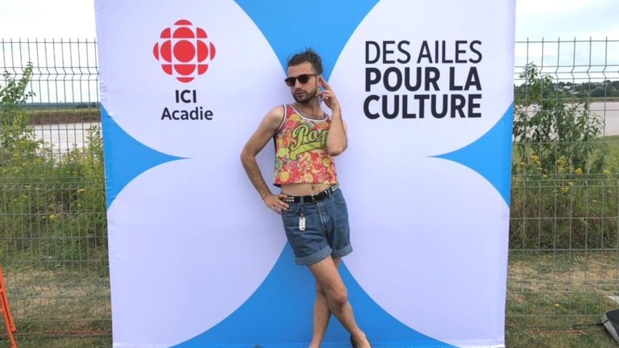 Xavier Gould pose devant un fond avec le libellé « ICI Acadie, des ailes pour la culture ». Xavier Gould pose devant un fond avec le libellé « ICI Acadie, des ailes pour la culture ».