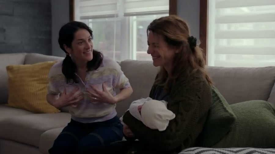 Les deux femmes rient assises sur un divan. L'une tient un bébé dans les bras.