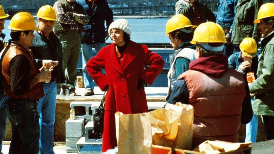 Une femme portant un bonnet blanc et un manteau rouge, les mains sur les hanches, au milieu d'un groupe d'ouvriers sur un toit. Une femme portant un bonnet blanc et un manteau rouge, les mains sur les hanches, au milieu d'un groupe d'ouvriers sur un toit.