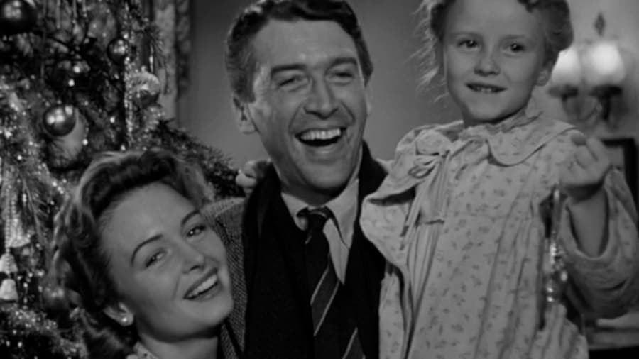Une femme, un homme avec une petite fille souriante dans les bras, devant un sapin de Noël.