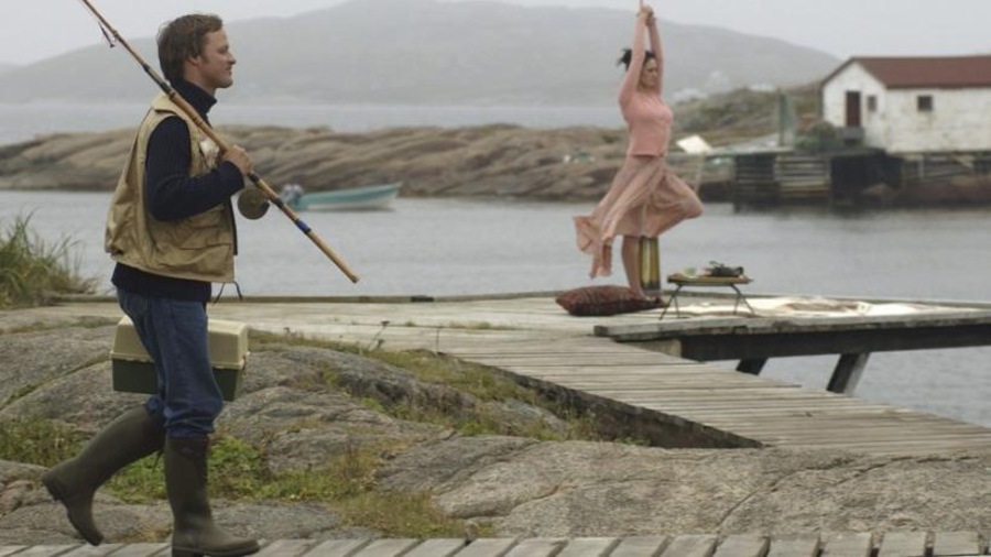 Un homme avec une canne à pêche marche sur un quai, et passe devant une femme en rose qui s'étire. Un homme avec une canne à pêche marche sur un quai, et passe devant une femme en rose qui s'étire.