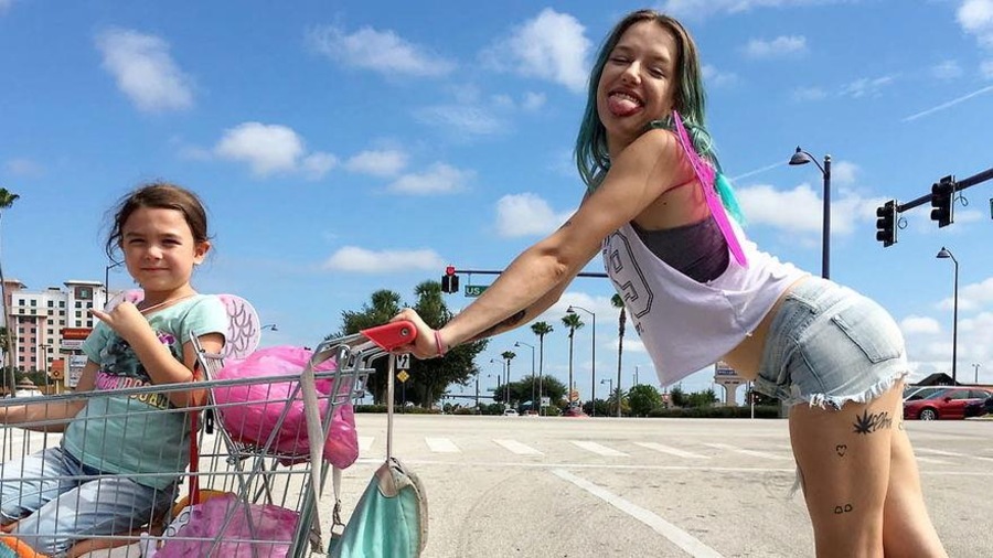 Une jeune femme en short tire la lange et tient un chariot dans lequel est assise une petite fille, sur un stationnement. Une jeune femme en short tire la lange et tient un chariot dans lequel est assise une petite fille, sur un stationnement.
