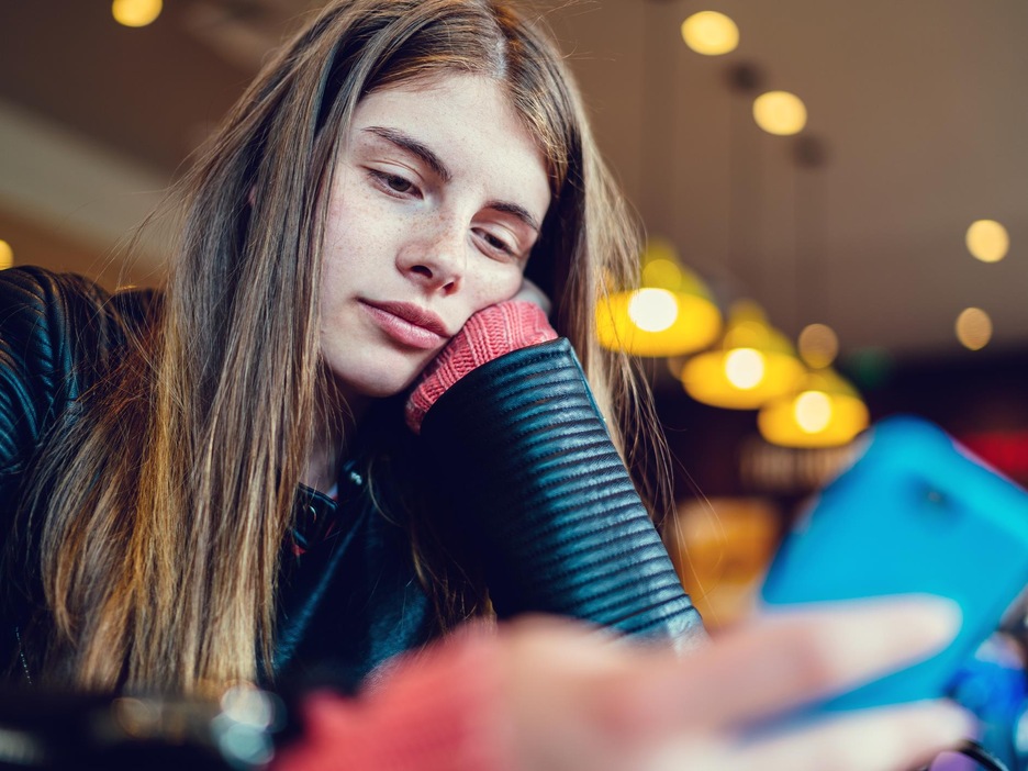 Une adolescente regarde son téléphone dans un café. Une adolescente regarde son téléphone dans un café.