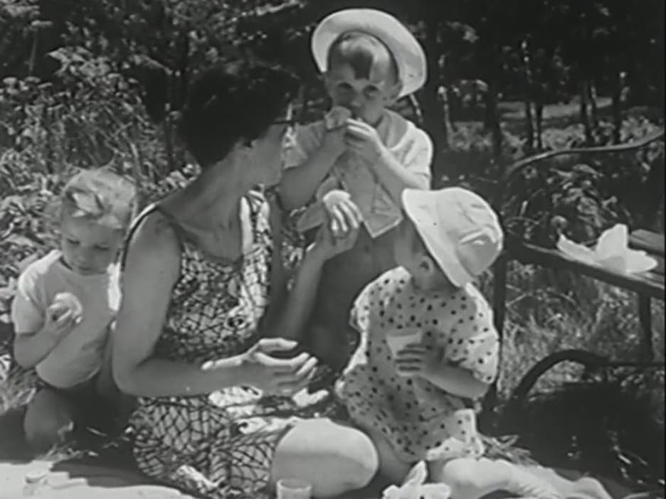Mère accroupie sur une nappe de pique-nique, entourée de trois enfants qui mangent des fruits. Mère accroupie sur une nappe de pique-nique, entourée de trois enfants qui mangent des fruits.