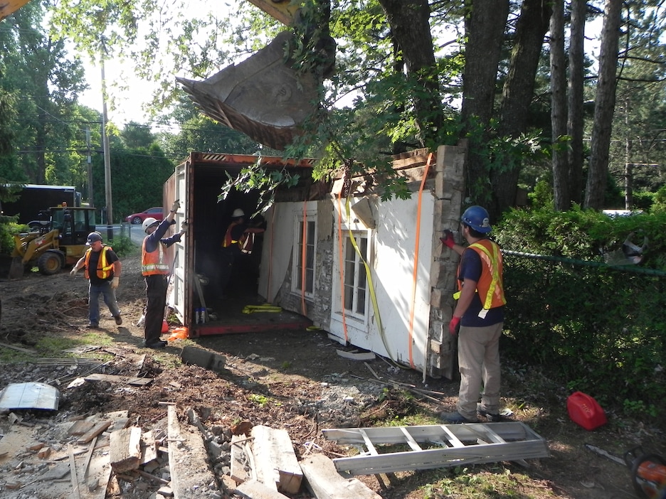 Des ouvriers embarquent dans un conteneur un mur avec deux fenêtres. Des ouvriers embarquent dans un conteneur un mur avec deux fenêtres.