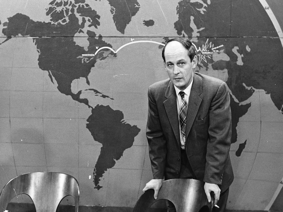 Debout devant une carte du monde,
l'animateur René Lévesque est appuyé au
dossier d'une chaise, une cigarette entre les
doigts. Debout devant une carte du monde,
l'animateur René Lévesque est appuyé au
dossier d'une chaise, une cigarette entre les
doigts.