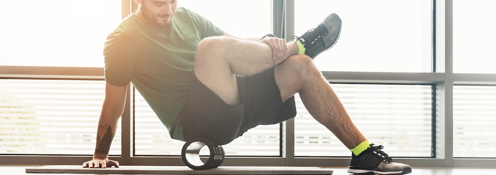 Sur le bord d'une fenêtre de salle de sports, un homme roule sur un cylindre sur un tapis d'entrainement. Sur le bord d'une fenêtre de salle de sports, un homme roule sur un cylindre sur un tapis d'entrainement.